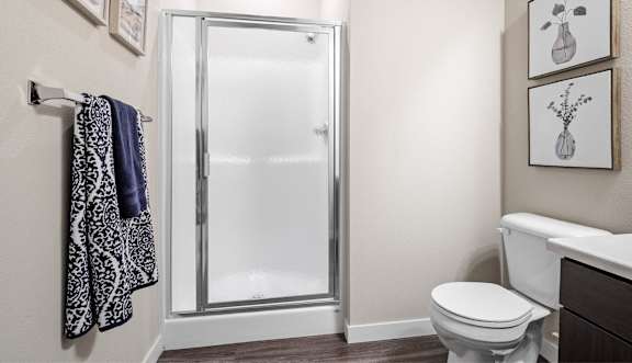 A bathroom with a toilet, a shower with a glass door, and towels hanging on a rack.
