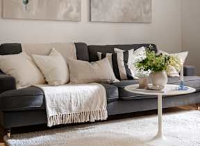 Cozy living room with a grey couch and white throw blanket representing comfortable living at Willow Creek Apartments.
