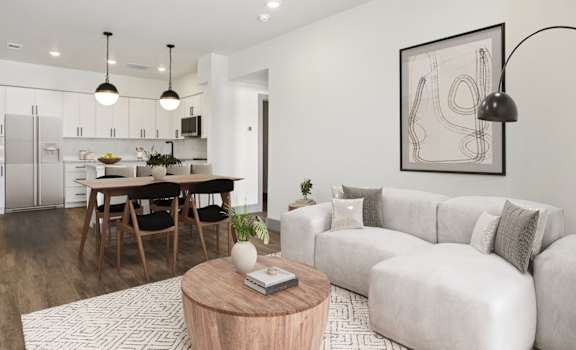 A modern living room with a grey sofa, wooden coffee table, and a dining table with chairs.