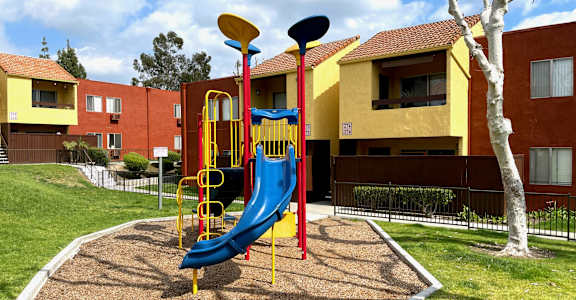 a playground in a yard with a blue slide at Brookhollow Apartments, West Covina , California