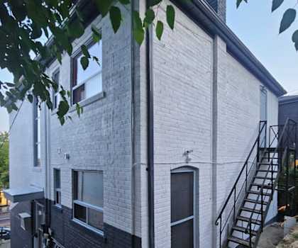 A white and black building with a black door and a black metal staircase.
