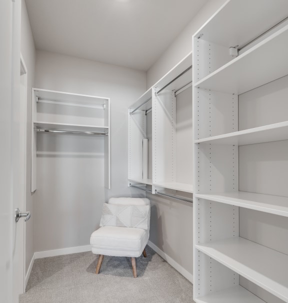 a walk in closet with white shelving and a white chair