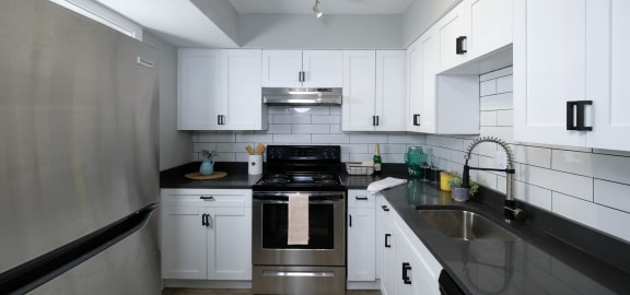 Kitchen in Mandarin Bay apartments in Jacksonville, FL with stainless steel electric appliances, white cabinets with black pulls, and white tile.