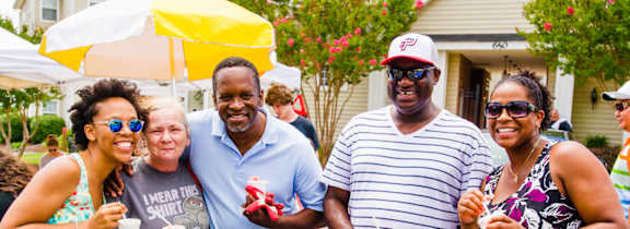 A group of people are standing together outside, holding drinks and smiling.