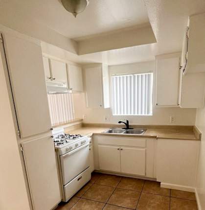 A kitchen with white appliances and brown tile flooring.