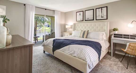 a bedroom with a bed and a desk with a chair in front of a sliding glass door