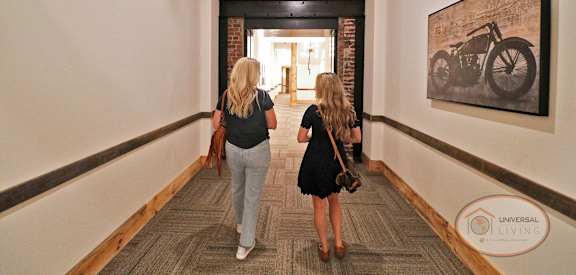 Two women walking down a hallway with a brick wall and a motorcycle picture on the wall.