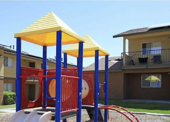 A playground with a yellow canopy and red and blue structure in front of apartment buildings.