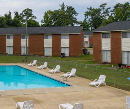 A pool surrounded by chairs and trees.