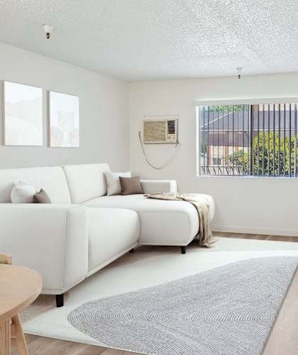 A white couch sits in a living room with a television on the wall.
