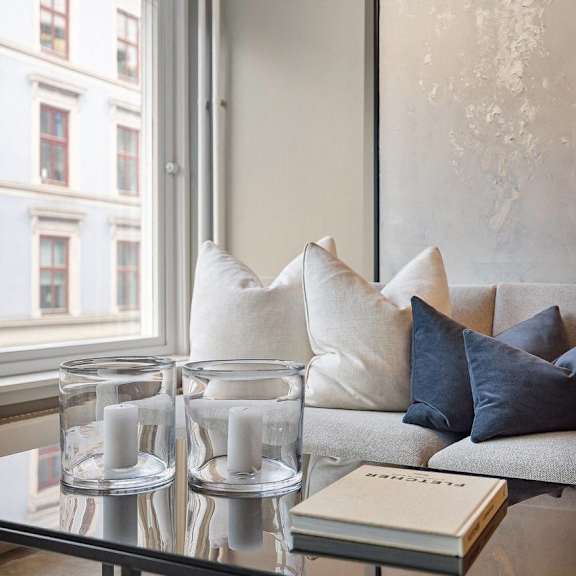 Living room with a couch, a table holding candles and a book, and a window in the background.