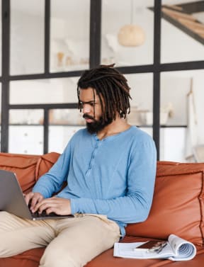 Man Sitting on Red Leather Couch Working on Laptop