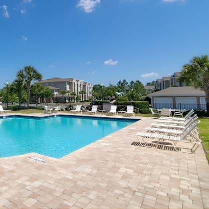 A swimming pool surrounded by a brick patio and lounge chairs.