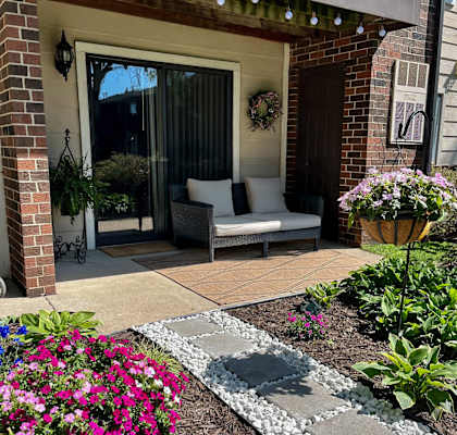 A patio with a couch and a table with a flower pot on the left and a flower pot on the right.