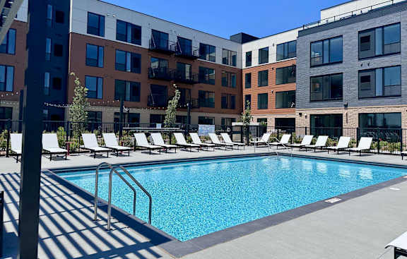 A pool surrounded by sun loungers in front of apartment buildings.