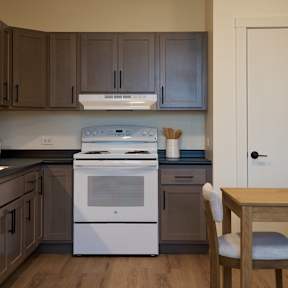 A white refrigerator stands in a kitchen with brown cabinets and a black countertop.