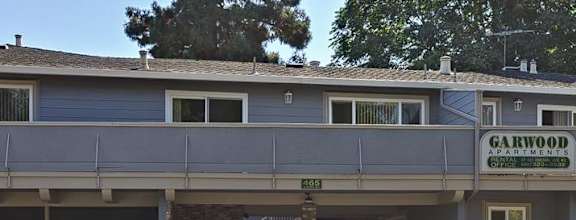A large tree stands in front of a two-story apartment building.