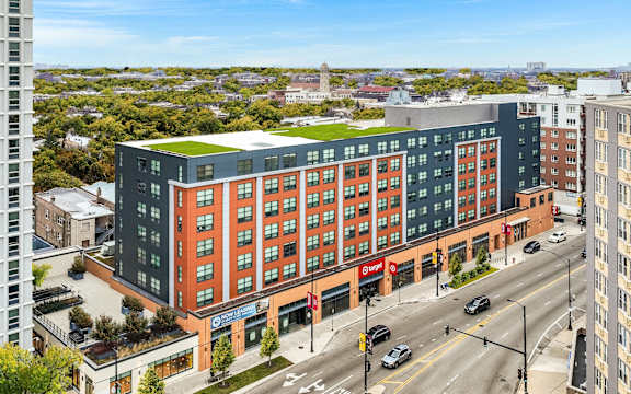 A large multi-story building with a green roof is situated on a busy street.