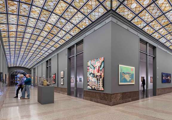 A group of people are walking through a hallway with art on the walls.