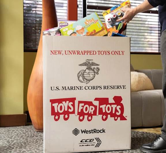 A man is handing over a box of unwrapped toys to the U.S. Marine Corps Reserve Toys for Tots program.