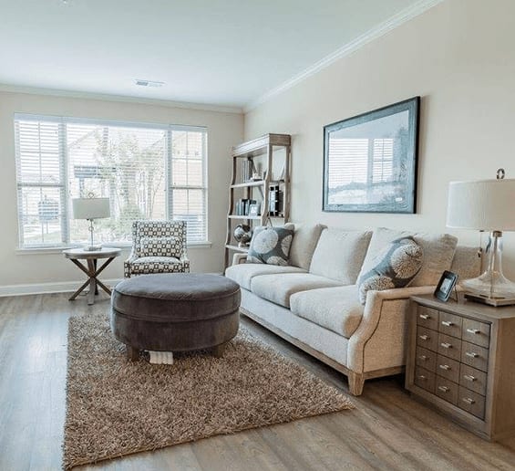 A living room with a white couch, a grey ottoman, and a brown rug.