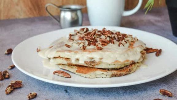 a plate of pancakes with syrup and nuts on a table