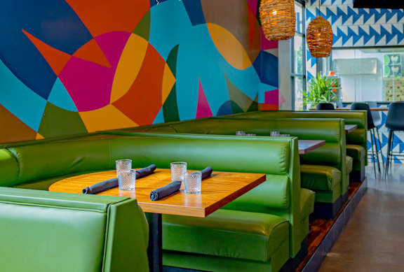 A restaurant with green booths and a colorful mural on the wall.