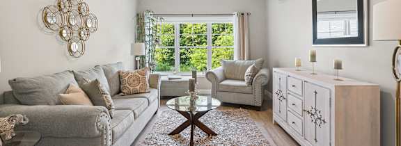 A living room with a grey couch, a wooden coffee table, and a large window with a view of greenery outside.
