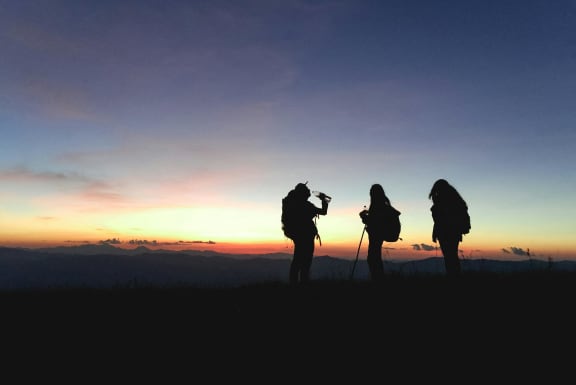 three people standing on a mountain at sunset
