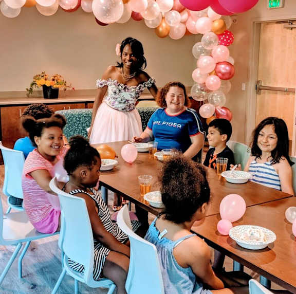 A group of people are sitting around a table with pink balloons.