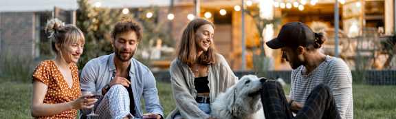 Four people sitting on the grass with a dog.