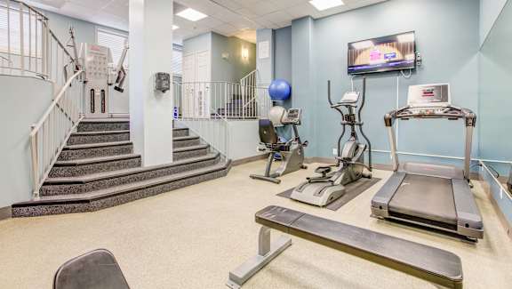 A gym with a staircase, treadmills, and exercise equipment.