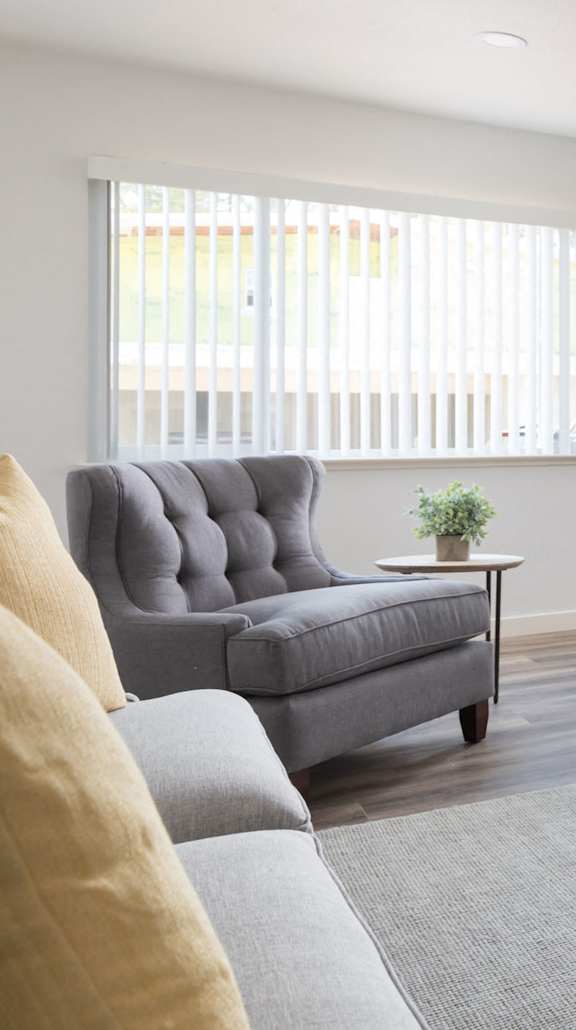A living room with a grey couch, a grey armchair, a small table, and a grey dresser.