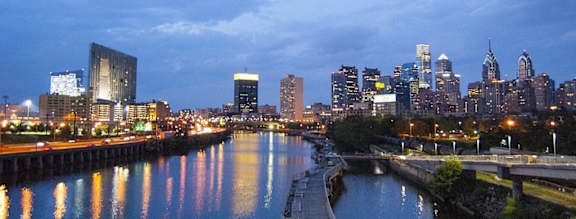 A city skyline at dusk with buildings reflecting in the water.