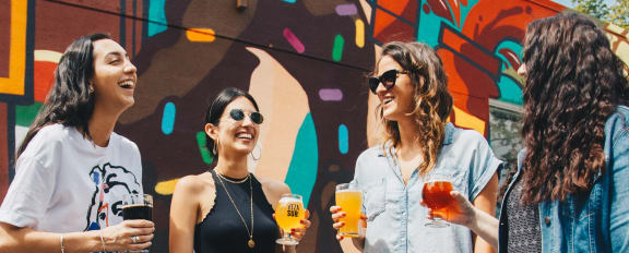 a group of women standing in front of a mural holding drinks