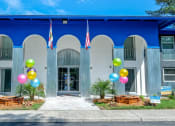 Thumbnail 21 of 23 - Jacksonville Mandarin Bay Apartments front office exterior. Front door is flanked by wood planters, colorful balloons, and the Florida and United States flags.