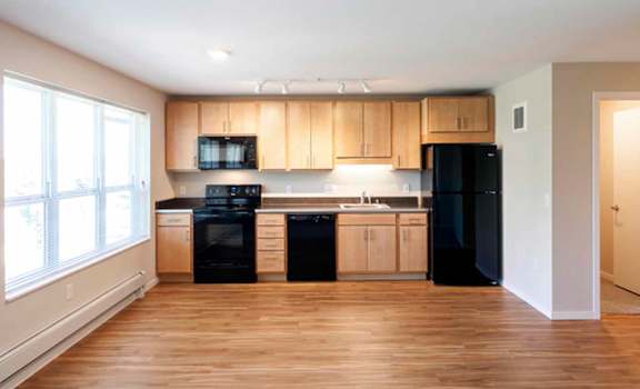 an empty living room with a kitchen in the background