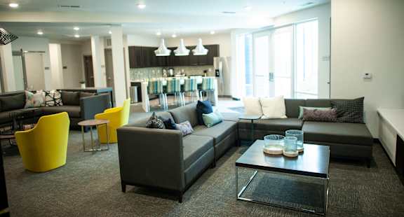 a living room with a kitchen in the background and a couch and chairs in the foreground