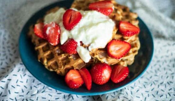 a plate of waffles with strawberries and whipped cream