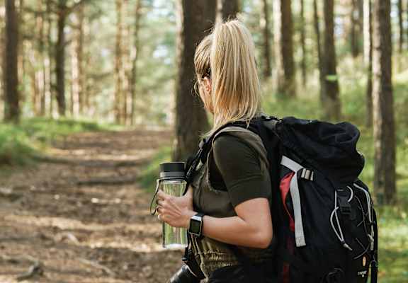 A woman with a backpack and a camera is standing on a forest path.