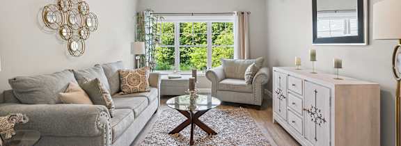 A living room with a grey couch, a wooden coffee table, and a large window with a view of greenery outside.