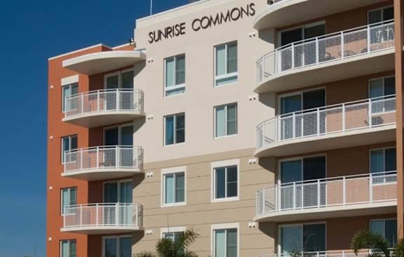 A Sunrise Commons apartment building with balconies and palm trees in front.