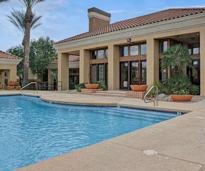 The turquoise outdoor pool with pool chairs, tables, and chairs with the apartments in the background at Mirador Apartment Homes, 