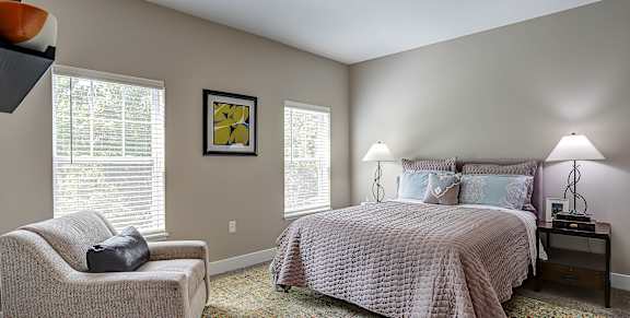 A bedroom with a bed, chair, and lamp.