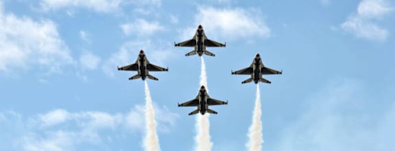 Four fighter jets flying in formation with smoke coming out of their tail.