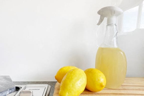 a bottle of lemon juice and three lemons on a cutting board