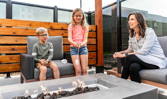 A woman and two children are sitting on a patio with a fire pit in front of them.