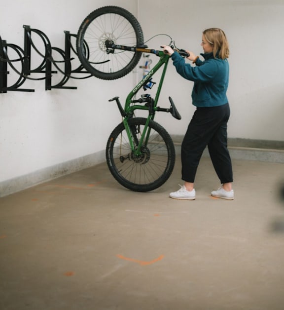 A woman is holding a bike in a room with a white wall.