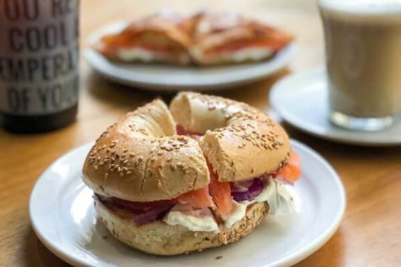 a bagel sandwich on a plate next to a cup of coffee