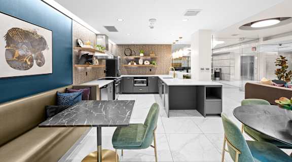 Community kitchen space with white counter tops,, grey cabinets, comfortable seating areas with marble tables and velvet chairs